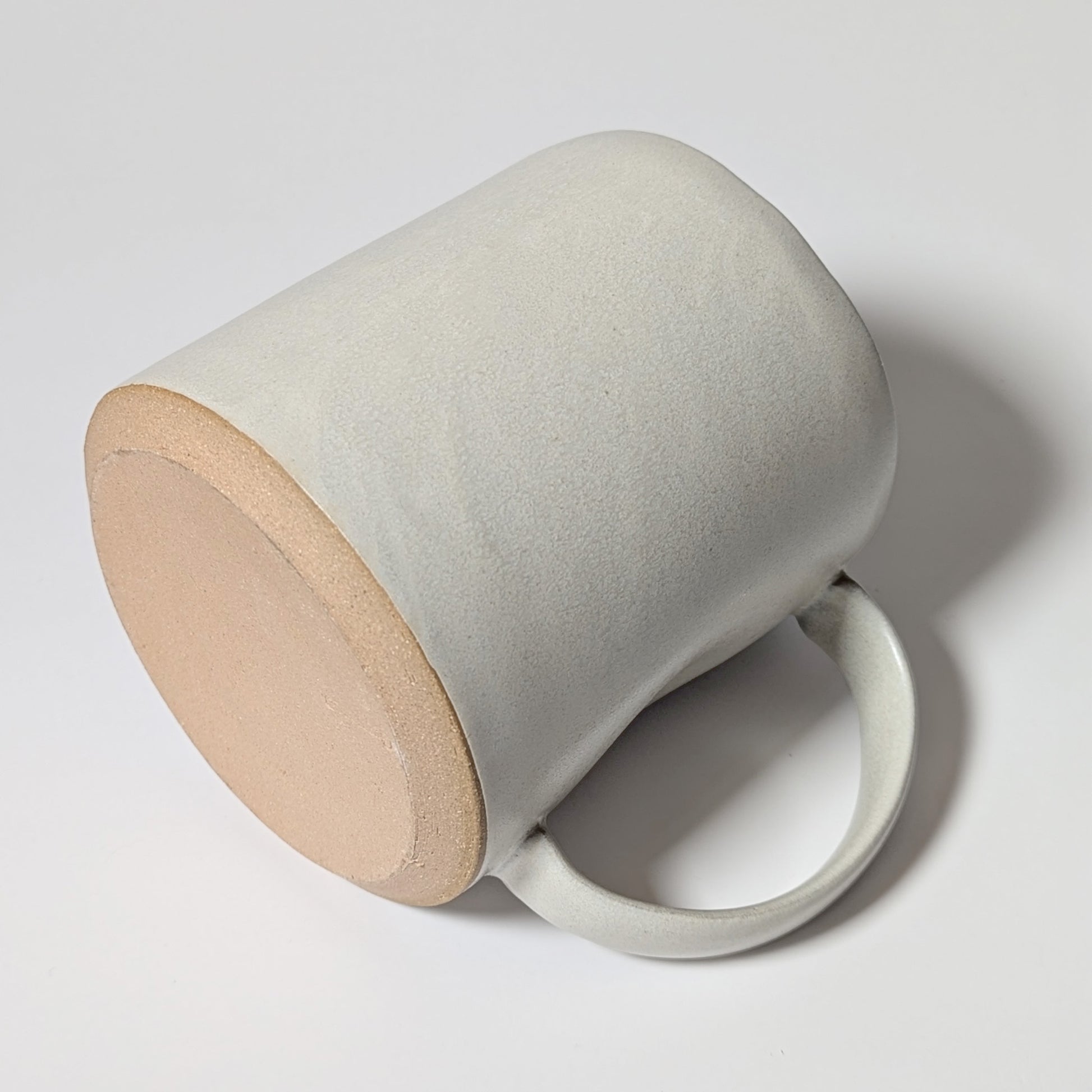 Off-white stoneware mug resting on its side, highlighting raw clay base and smooth handle