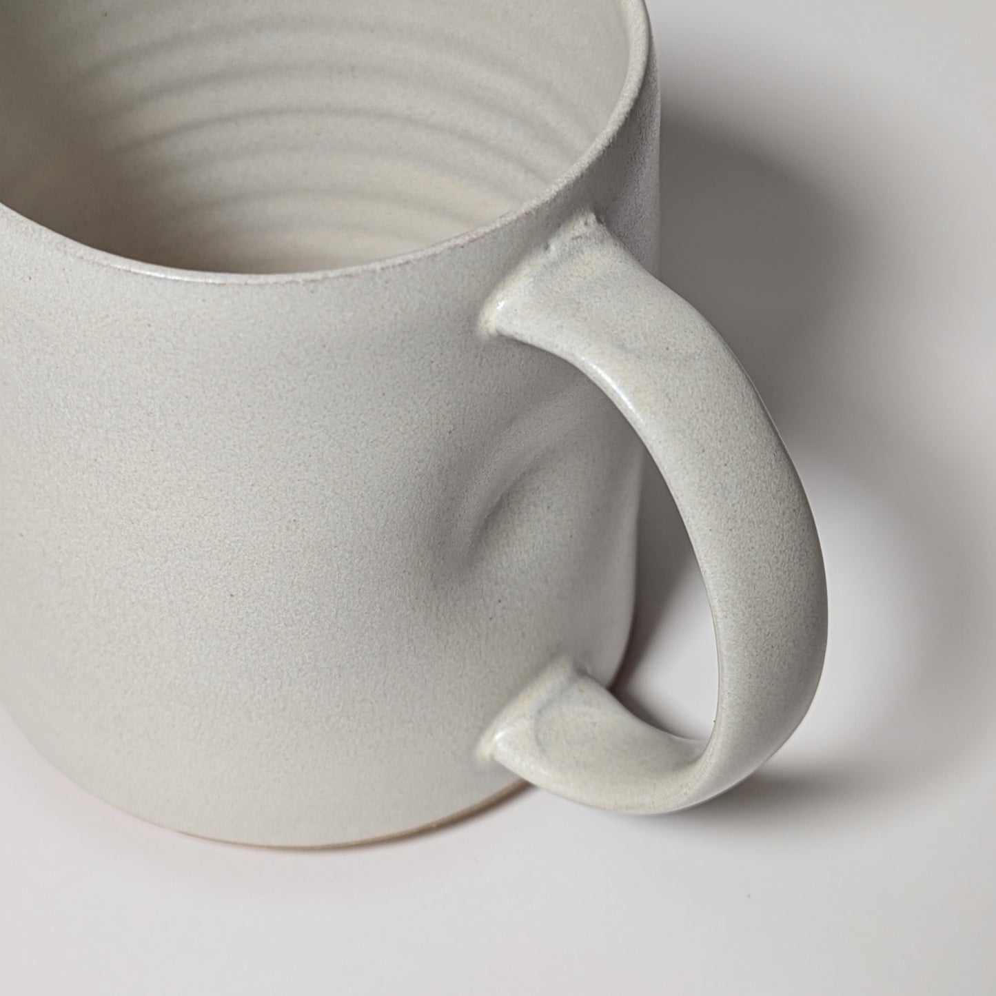 Angled view of off-white handmade mug emphasizing soft curves and grounded silhouette