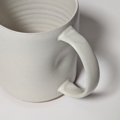 Angled view of off-white handmade mug emphasizing soft curves and grounded silhouette