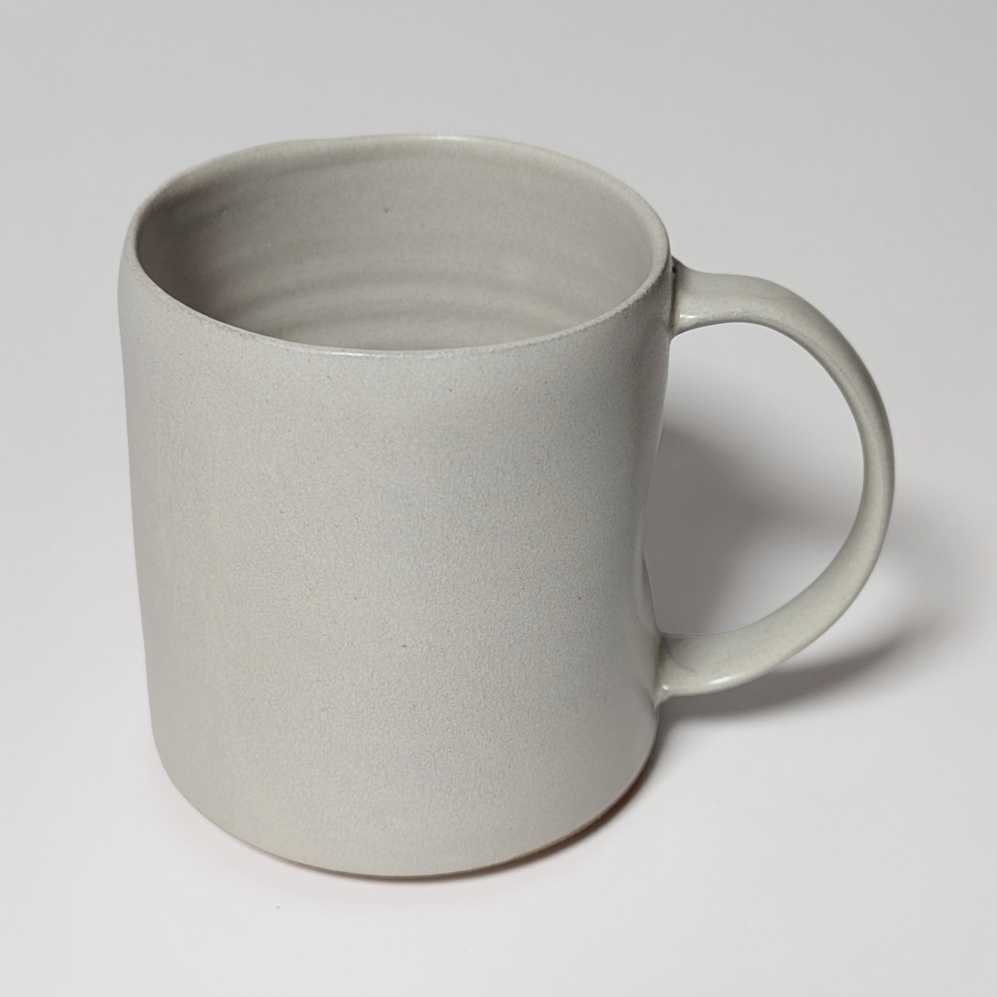 Front view of off-white stoneware mug with matte glaze and gently tapered lip