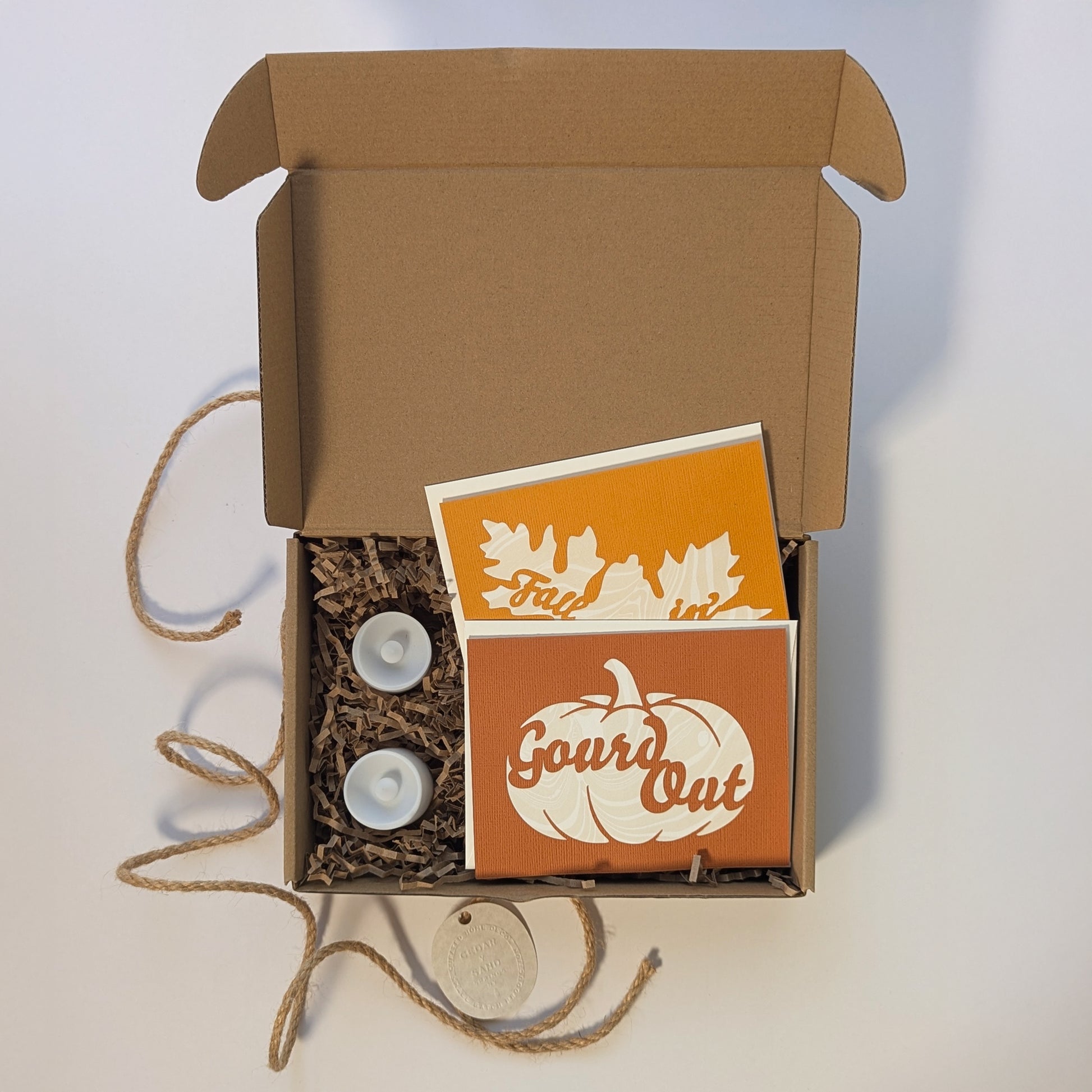 Boxed presentation of the “Gourd Out & Fallin’” lantern card set, showing two cut-out notecards, envelopes, and LED tealights arranged inside kraft packaging.