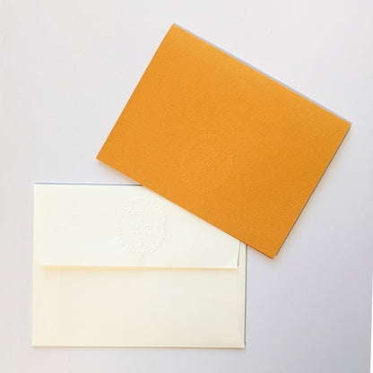 Reverse side of butternut colored notecard and natural colored envelope, both with the CEDAR Y SAND embossed insignia.