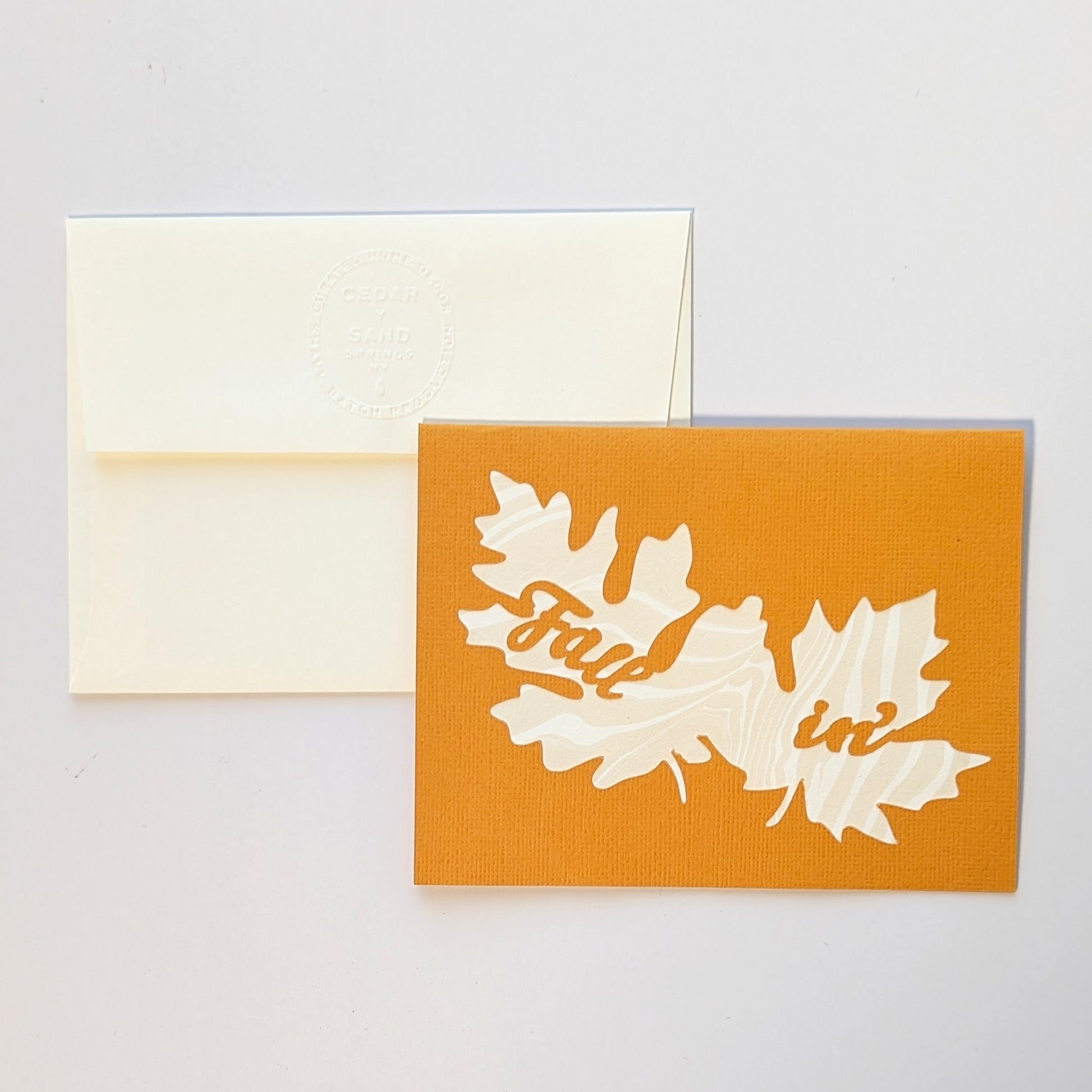 Paper cut Fallin' notecard in butternut color with embossed CEDAR Y SAND insignia on reverse of envelope