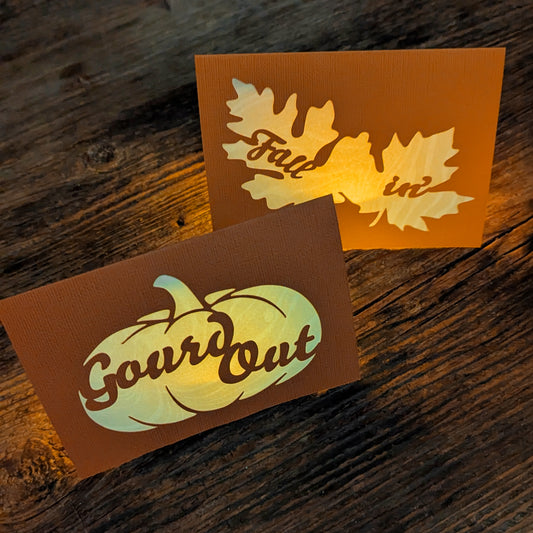 “Gourd Out & Fallin’” lantern notecards illuminated with LED tealights, showing the marbled paper glowing softly through the cut-out pumpkin and leaf designs.