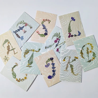Assorted pressed flower initial notecards on Suminagashi marbled paper, handmade botanical stationery collection by CEDAR Y SAND
