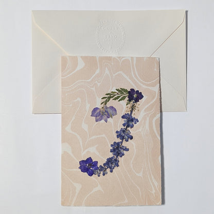 blush Suminagashi marbled background with deckled edges, paired with embossed CEDAR Y SAND envelope in premium Fabriano Medioevalis paper.