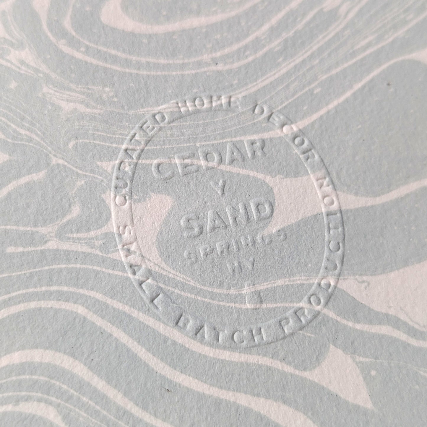 Embossed CEDAR Y SAND insignia on Suminagashi marbled Fabriano Medioevalis paper, highlighting artisanal details