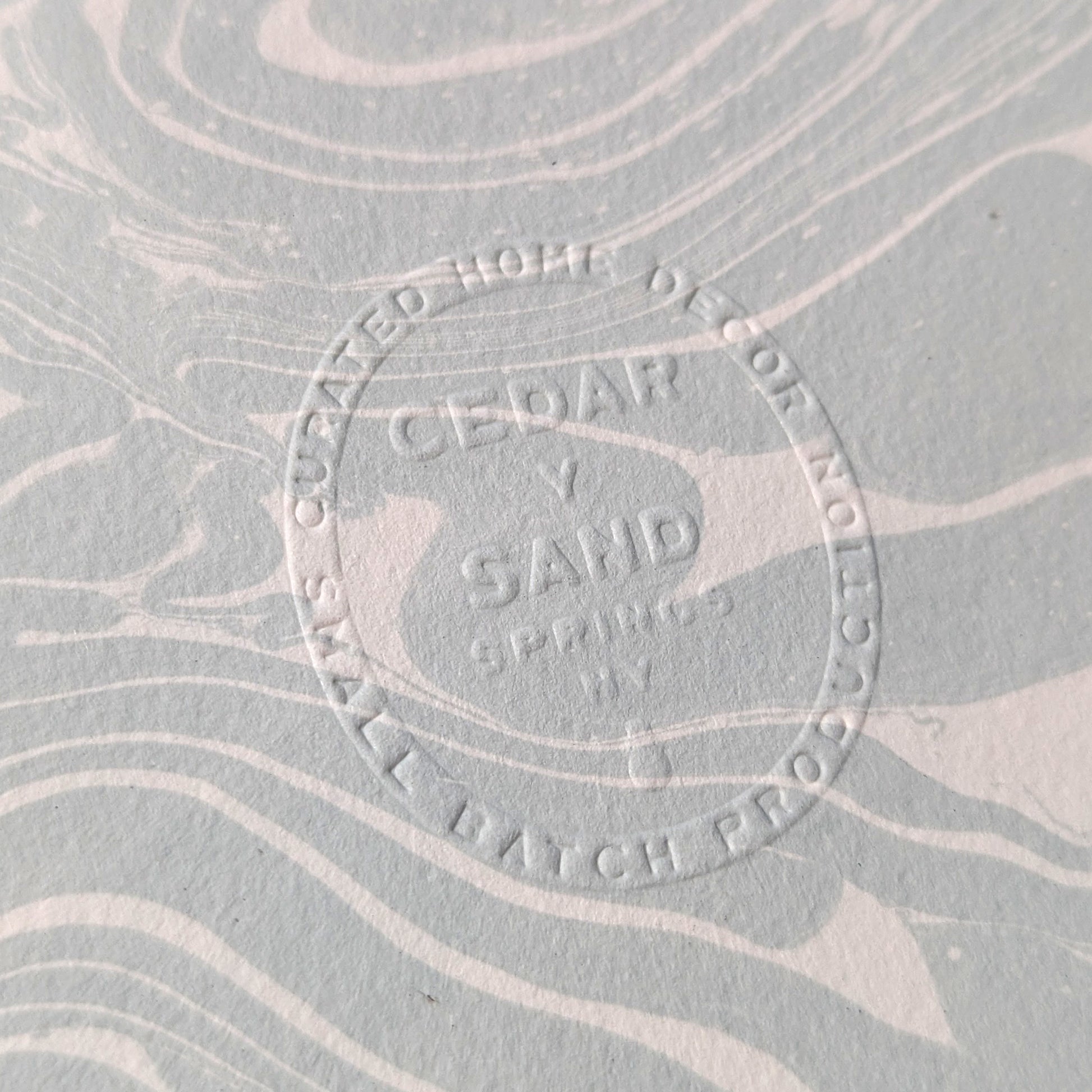 Embossed CEDAR Y SAND insignia on Suminagashi marbled Fabriano Medioevalis paper, highlighting artisanal details
