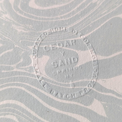 Embossed CEDAR Y SAND insignia on Suminagashi marbled Fabriano Medioevalis paper, highlighting artisanal details