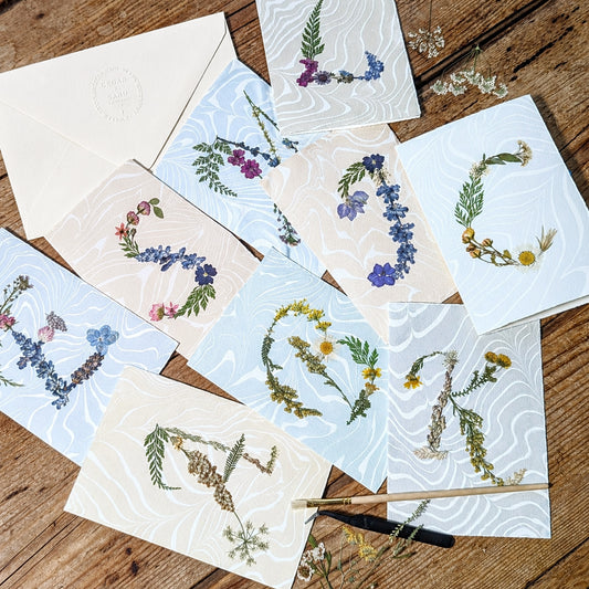 Assorted pressed flower initial notecards on Suminagashi marbled paper, handmade botanical stationery collection by CEDAR Y SAND