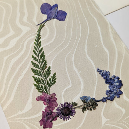 Pressed flower “L” initial notecard on hand-marbled Suminagashi paper, featuring purple and pink botanicals on premium Fabriano Medioevalis cardstock