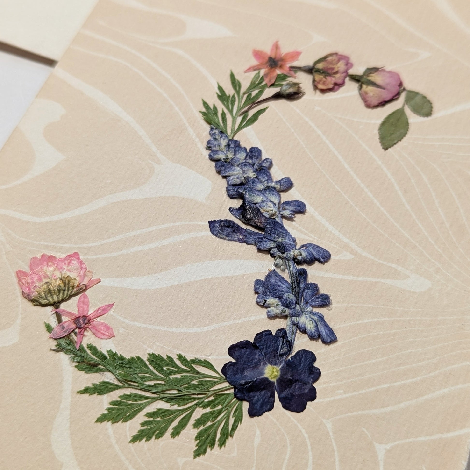 Pressed floral “S” initial notecard with blue and pink flowers on marbled Suminagashi background, handmade on Fabriano Medioevalis paper