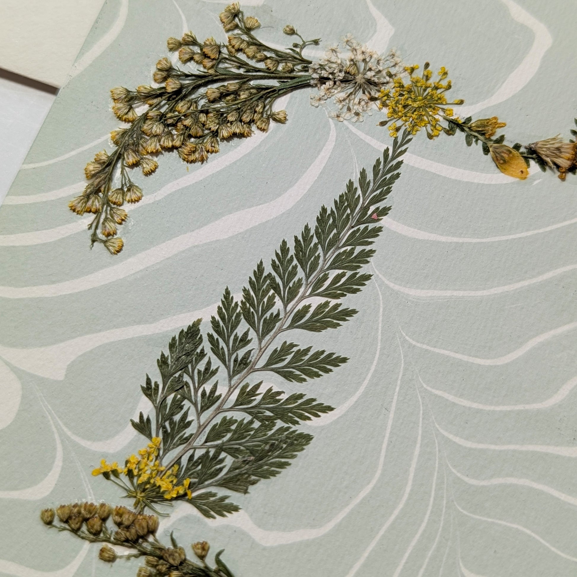 Pressed flower “T” initial notecard with yellow and white wildflowers on blue marbled Suminagashi paper, handcrafted on Fabriano cardstock