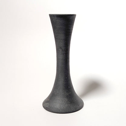 A single handcrafted black clay candle taper holder stands against a white backdrop. The wheel-thrown form shows subtle ridges and a matte, stone-like texture, highlighting its modern organic silhouette.