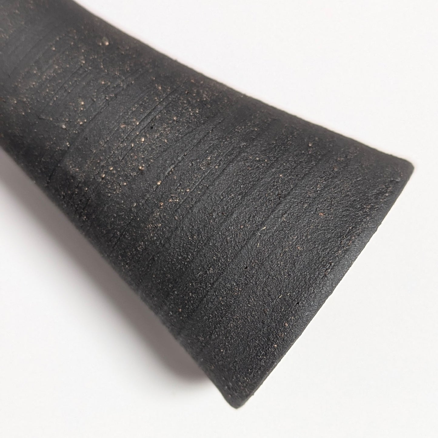 Macro detail of the black clay surface showing rustic speckling and circular ridges from the wheel-throwing process, emphasizing the tactile, hand-finished texture.