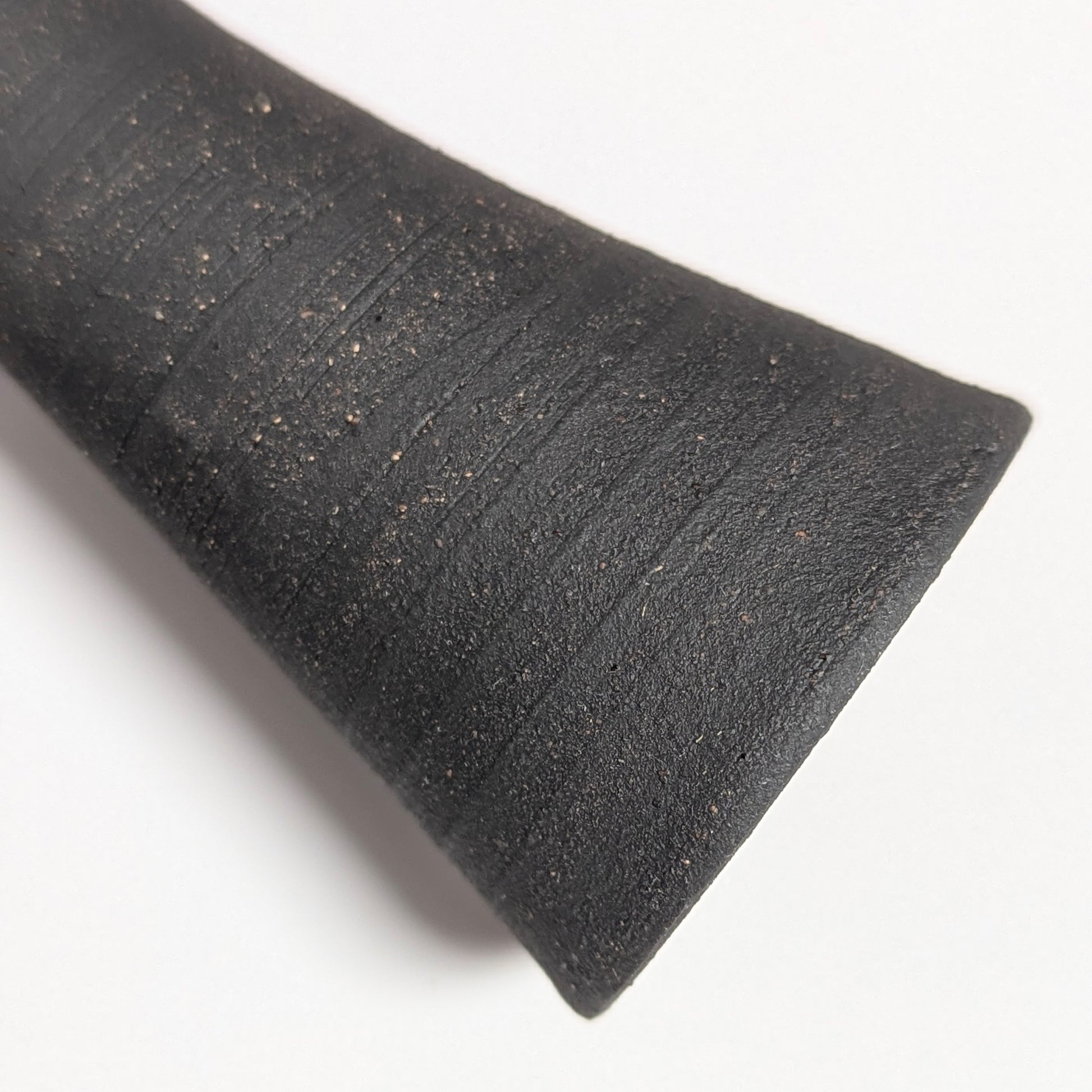 Macro detail of the black clay surface showing rustic speckling and circular ridges from the wheel-throwing process, emphasizing the tactile, hand-finished texture.