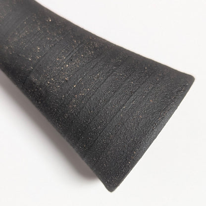 Macro detail of the black clay surface showing rustic speckling and circular ridges from the wheel-throwing process, emphasizing the tactile, hand-finished texture.