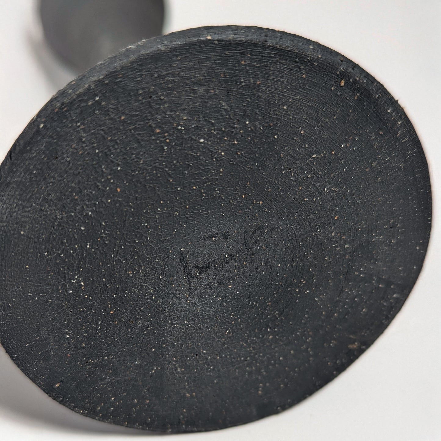 Bottom view of the handcrafted black clay candle holder showing the artist’s hand-signed signature impressed into the textured clay base.