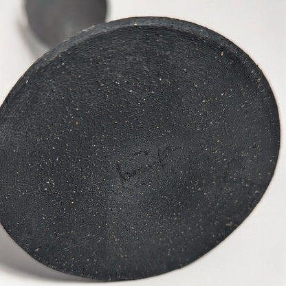 Bottom view of the handcrafted black clay candle holder showing the artist’s hand-signed signature impressed into the textured clay base.