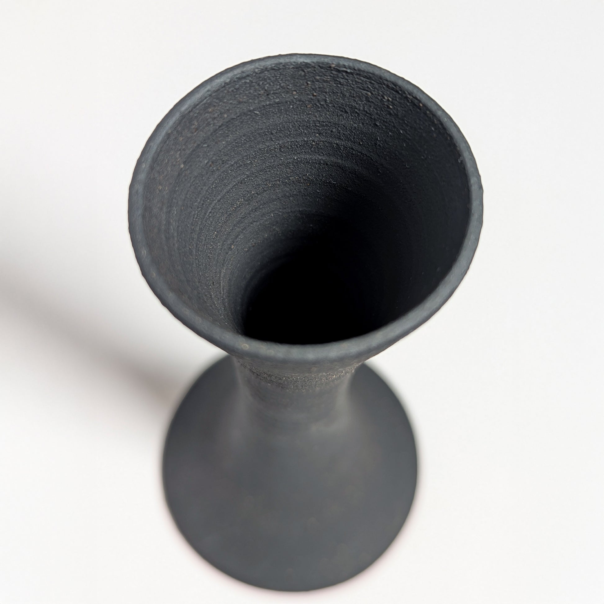 Looking down into the open mouth of the black clay candle holder, the interior reveals smooth throwing lines and a deep matte finish with natural texture variations.