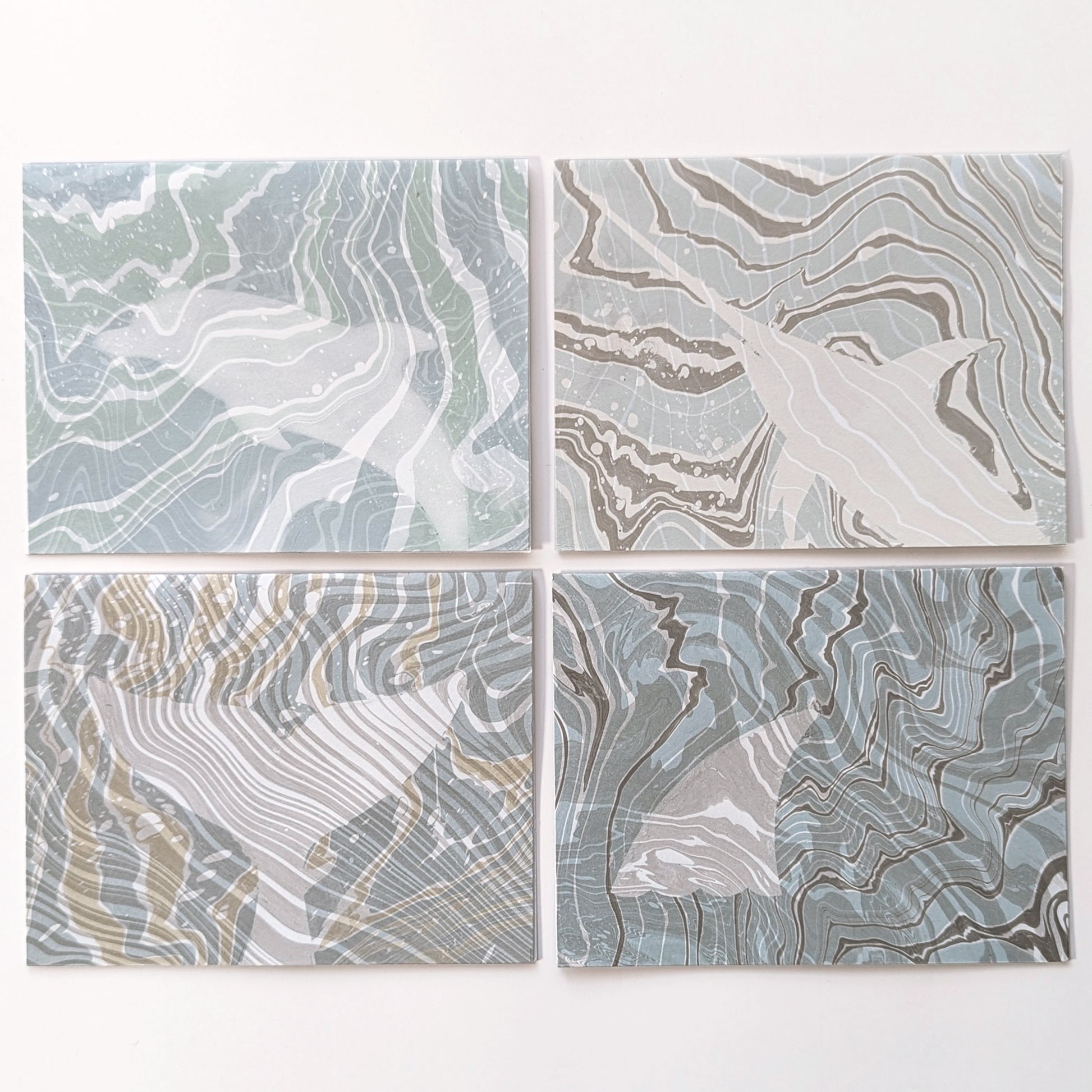 Set of four Marine Fauna Suminagashi notecards from the Fin Series, each featuring hand-marbled backgrounds with masked silhouettes of marine life: dolphin, swordfish, whale tail, and shark fin.