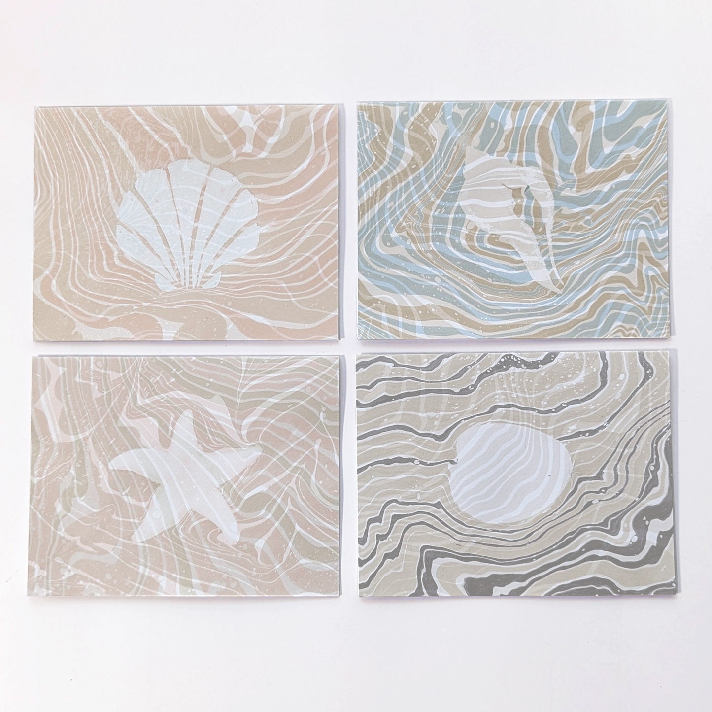 Set of four Marine Fauna Suminagashi notecards featuring scallop, whelk, starfish, and clam designs with hand-marbled suminagashi backgrounds.