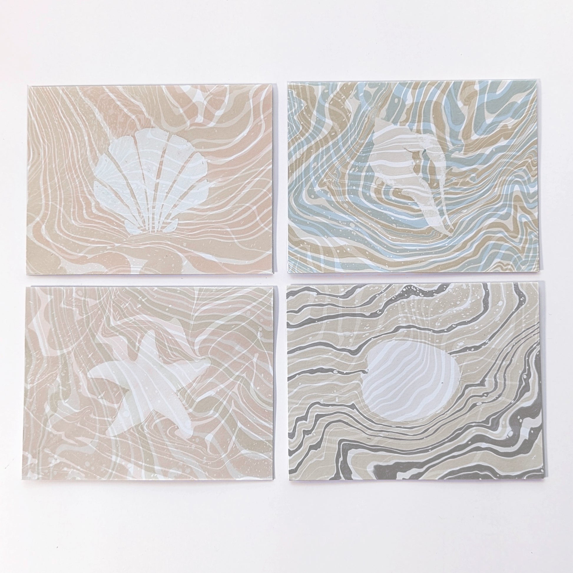 Set of four Marine Fauna Suminagashi notecards featuring scallop, whelk, starfish, and clam designs with hand-marbled suminagashi backgrounds.