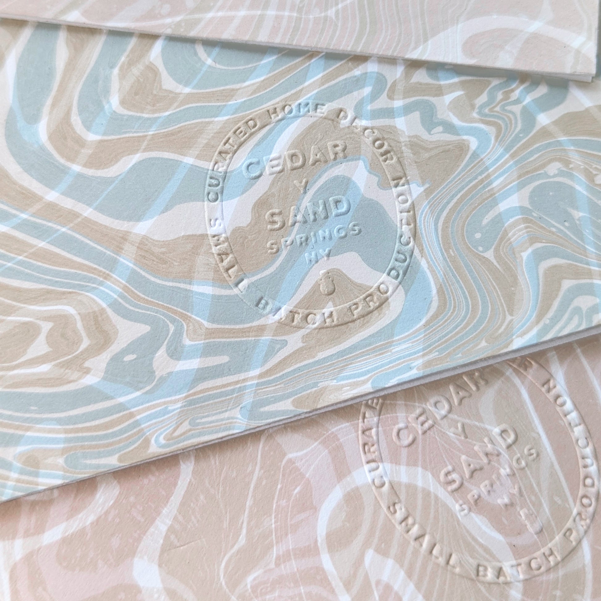 Close-up of embossed Cedar Y Sand insignia on the back of a Marine Fauna Sea Life notecard with marbled suminagashi detail.