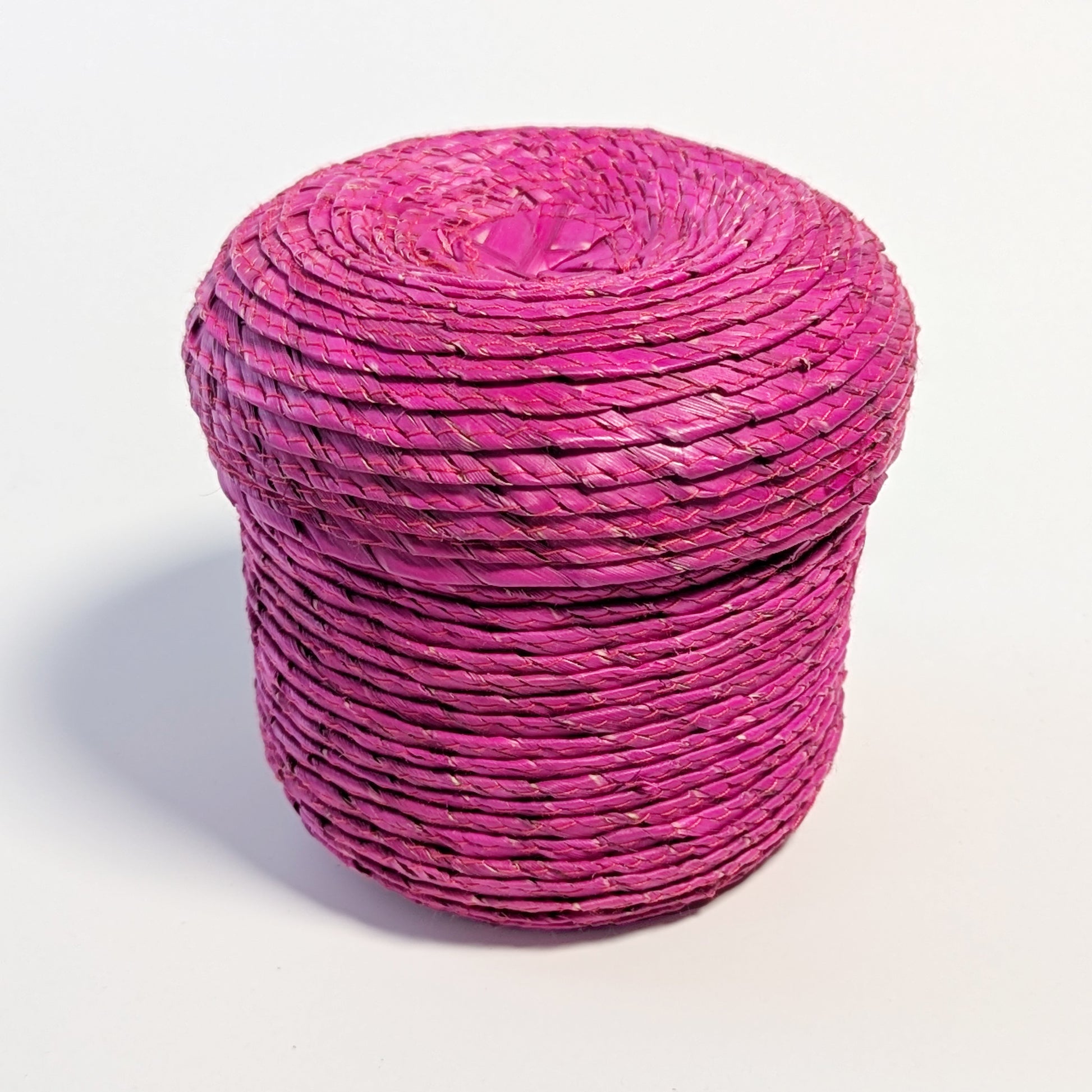 Lidded magenta palm leaf woven basket, on a white surface.