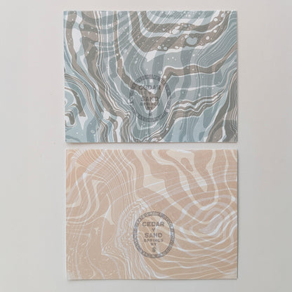 Back of Moonset and Sunrise Suminagashi notecards featuring flowing marbled designs and gray-stamped CEDAR Y SAND insignia.