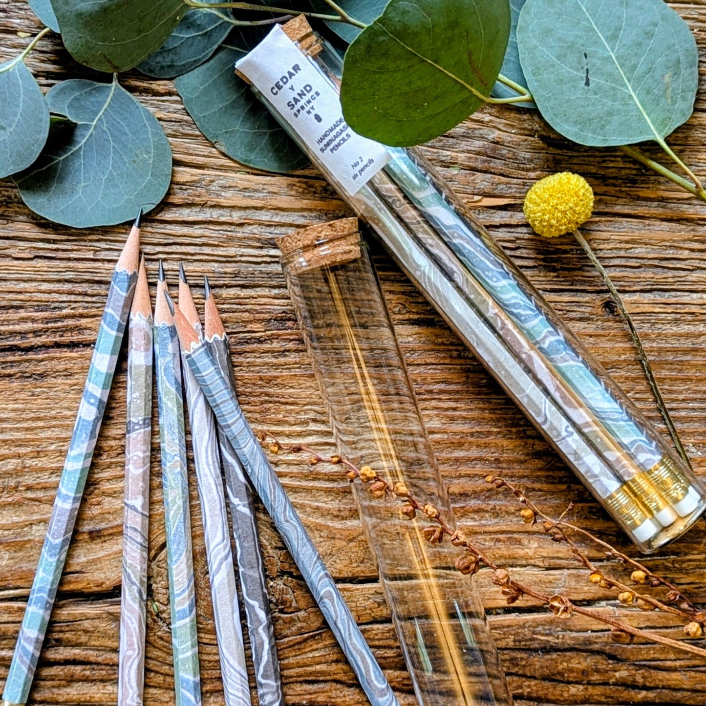 marble wrapped pencils displayed on a rustic wooden table with glass test tube with aa cork lid as packaging.