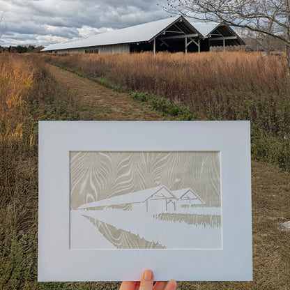 Hand-cut paper silhouette of the Parrish Art Museum displayed outdoors against the real museum landscape, featuring marbled suminagashi background.