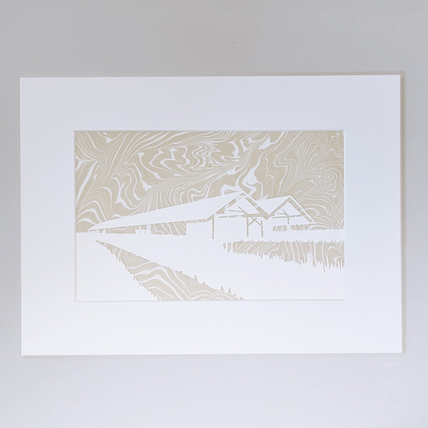 Paper cut silhouette of Parrish Art Museum over wheat-colored suminagashi marbled paper, matted in white.