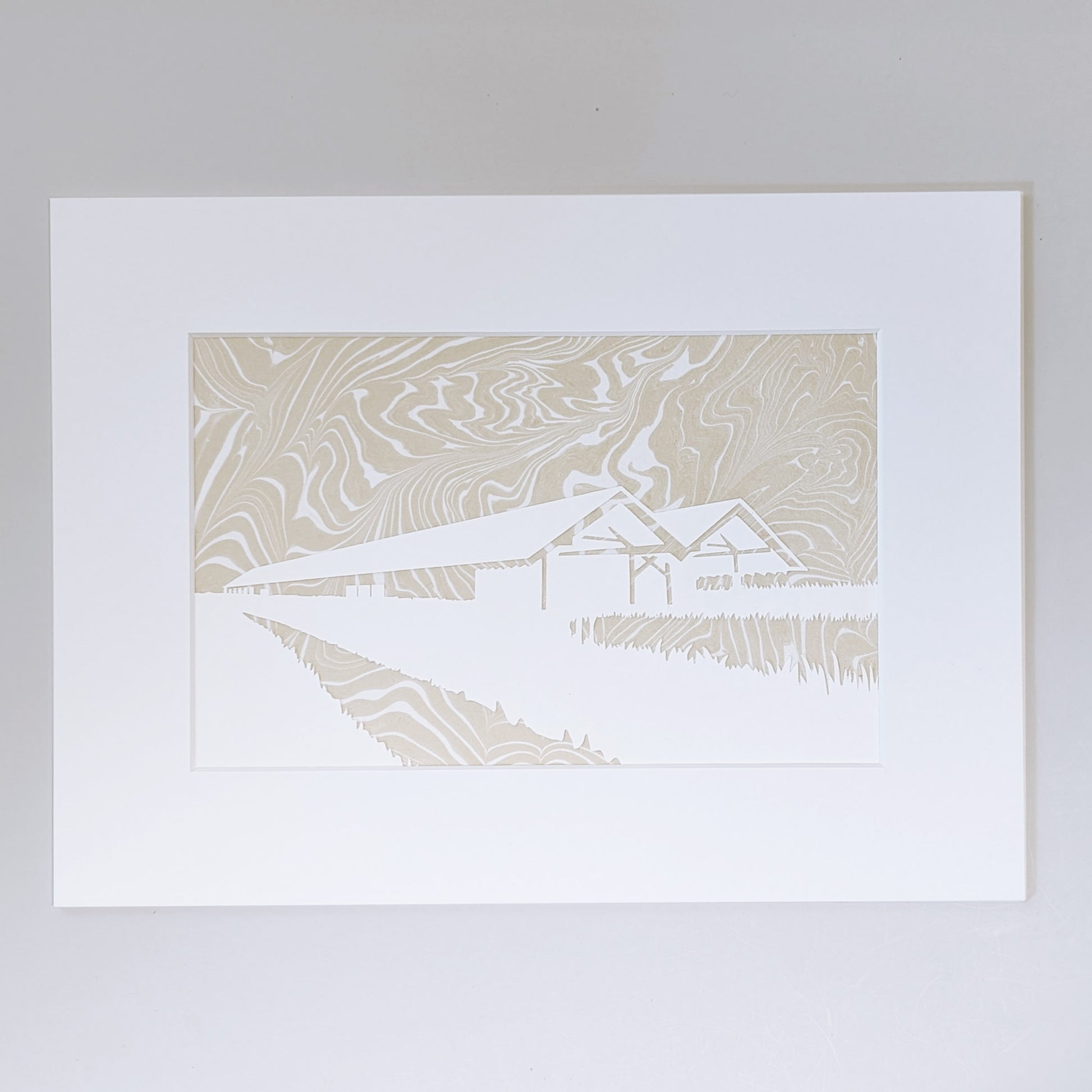 Paper cut silhouette of Parrish Art Museum over wheat-colored suminagashi marbled paper, matted in white.