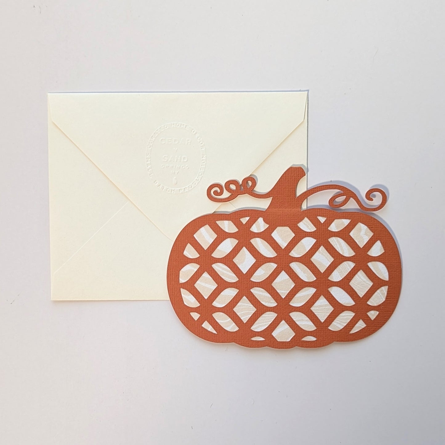 Hand-cut pumpkin lattice notecard with marbled paper backing beside embossed envelope on neutral background.