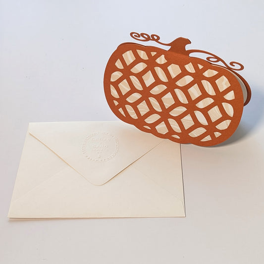 Front view standing beside embossed envelope on white background.
Alt: Pumpkin Lattice Notecard with cream envelope featuring CEDAR Y SAND embossed insignia.