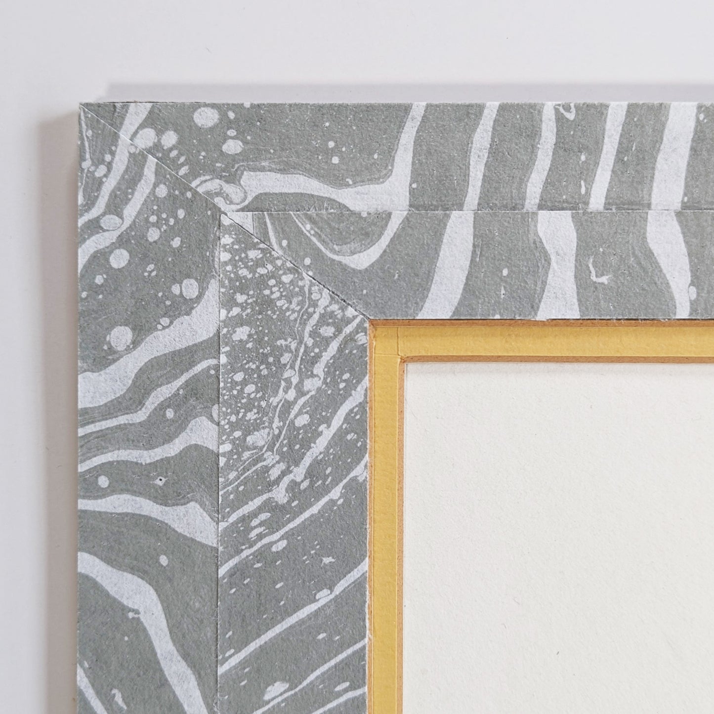 Close-up of corner showing gray suminagashi-marbled Hosho mat, golden inner liner, and clean archival mounting.