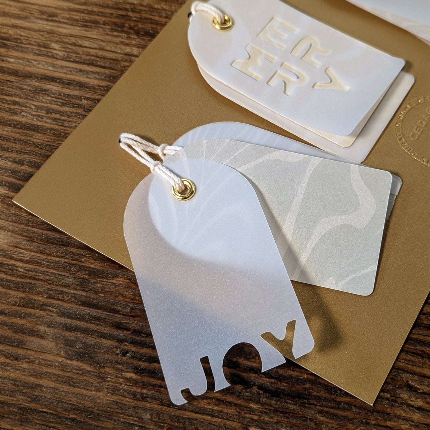 Close-up of the JOY vellum gift tag showing the pearlized Suminagashi marbled layer beneath the cut-out lettering.”