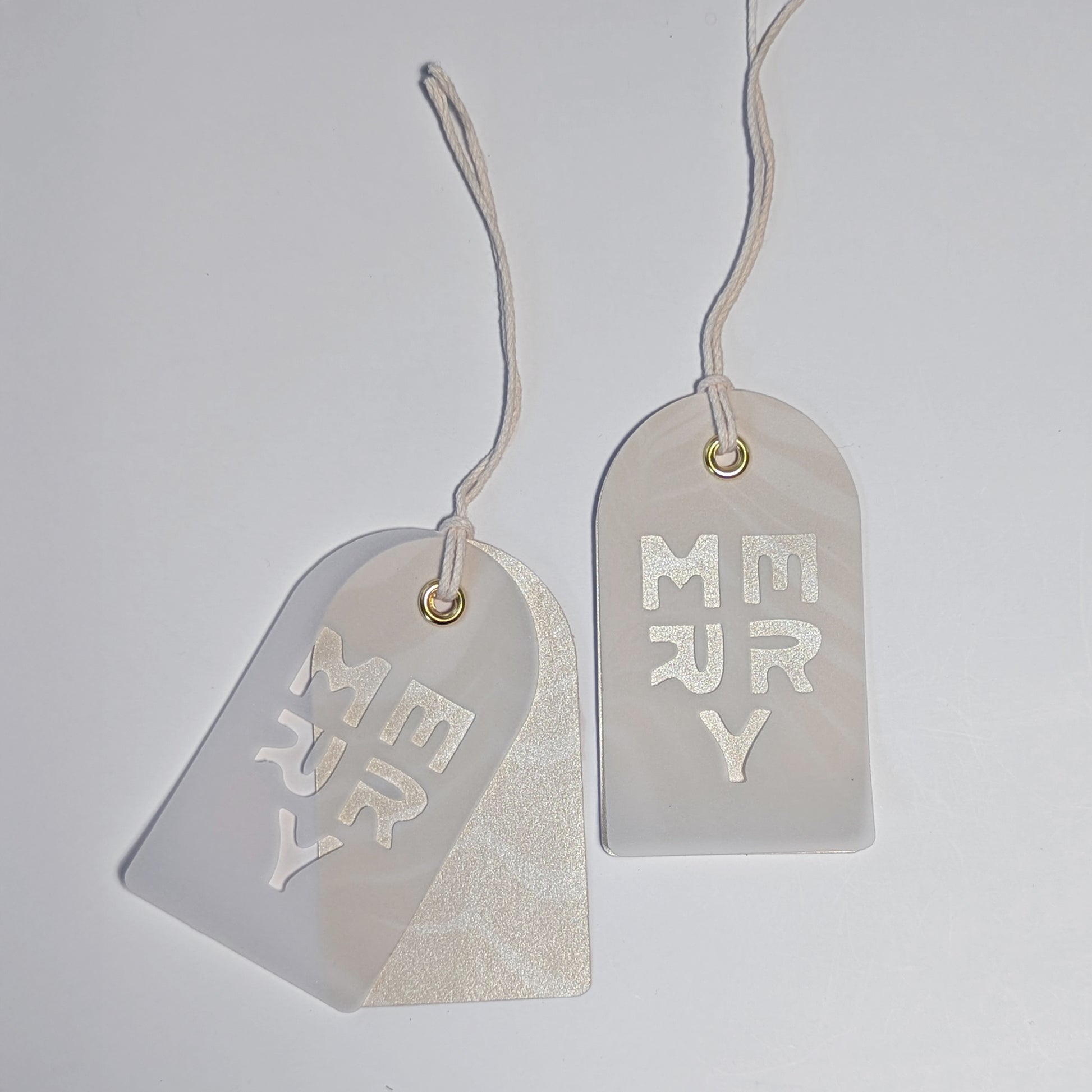 A pair of MERRY cut-out vellum gift tags layered over champagne-toned Suminagashi marbled paper.