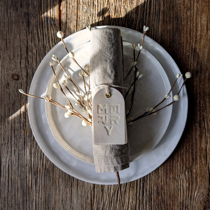 MERRY Suminagashi gift tag tied around a linen napkin on a white plate with winter berry branches arranged as a festive place setting.