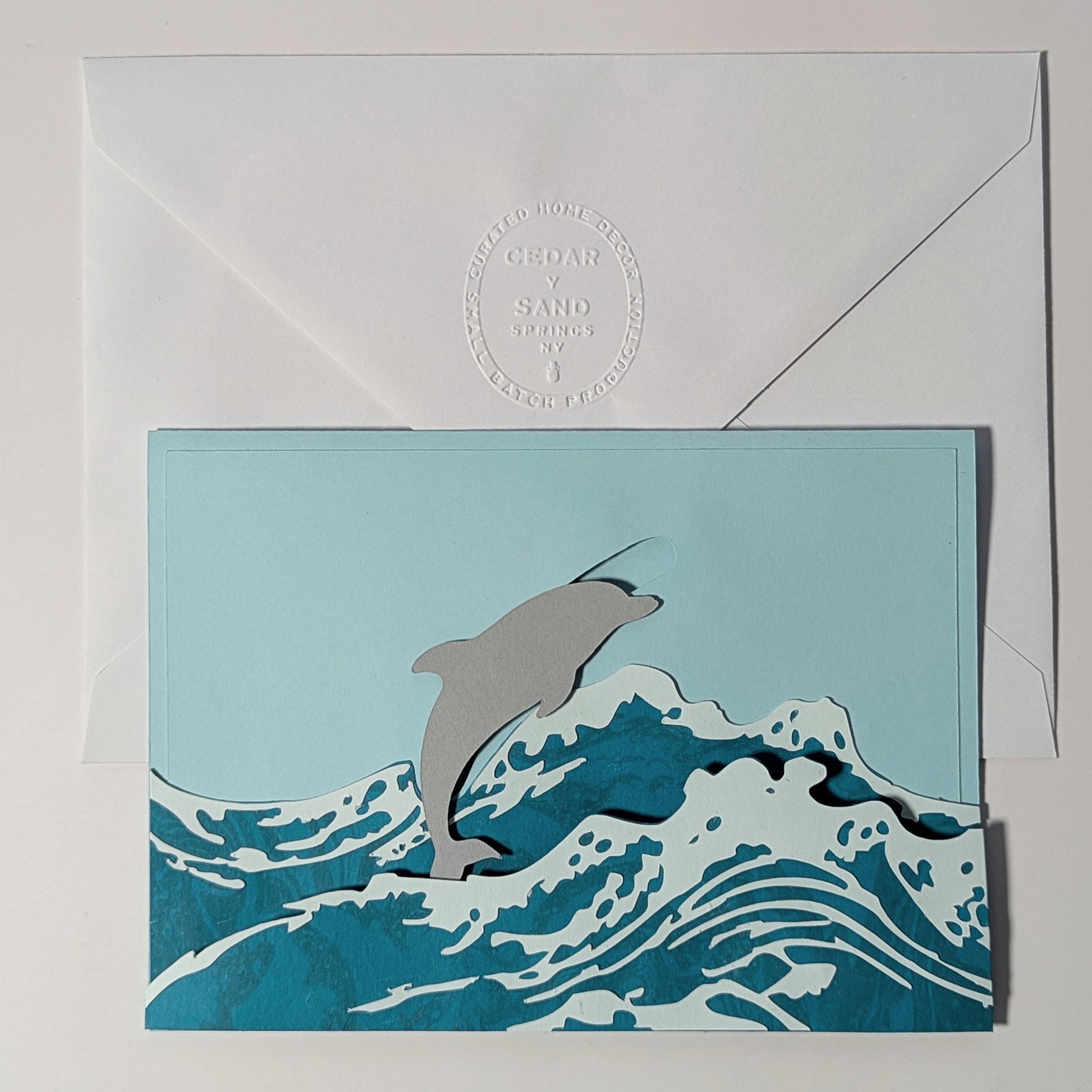 Surfin’ Flipper slider notecard with dolphin leaping through marbled waves, paired with insignia embossed envelope.