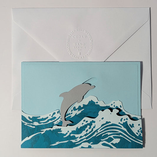 Surfin’ Flipper slider notecard with dolphin leaping through marbled waves, paired with insignia embossed envelope.