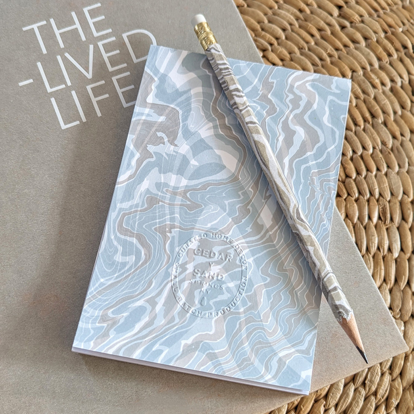 coastal hued marbled notepad with a marble wrapped pencil resting on a book