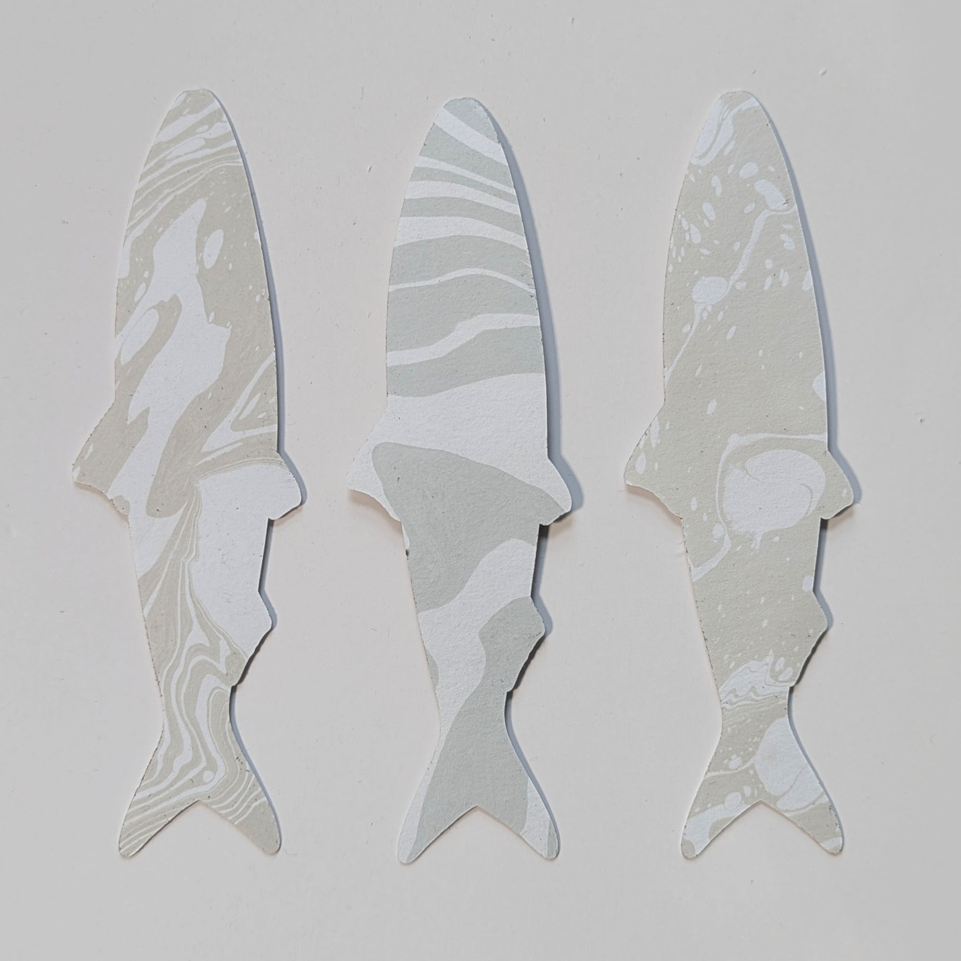 Reverse side of three handmade sardine bookmarks featuring unique muted neutral & gray hand-marbled Suminagashi paper patterns.