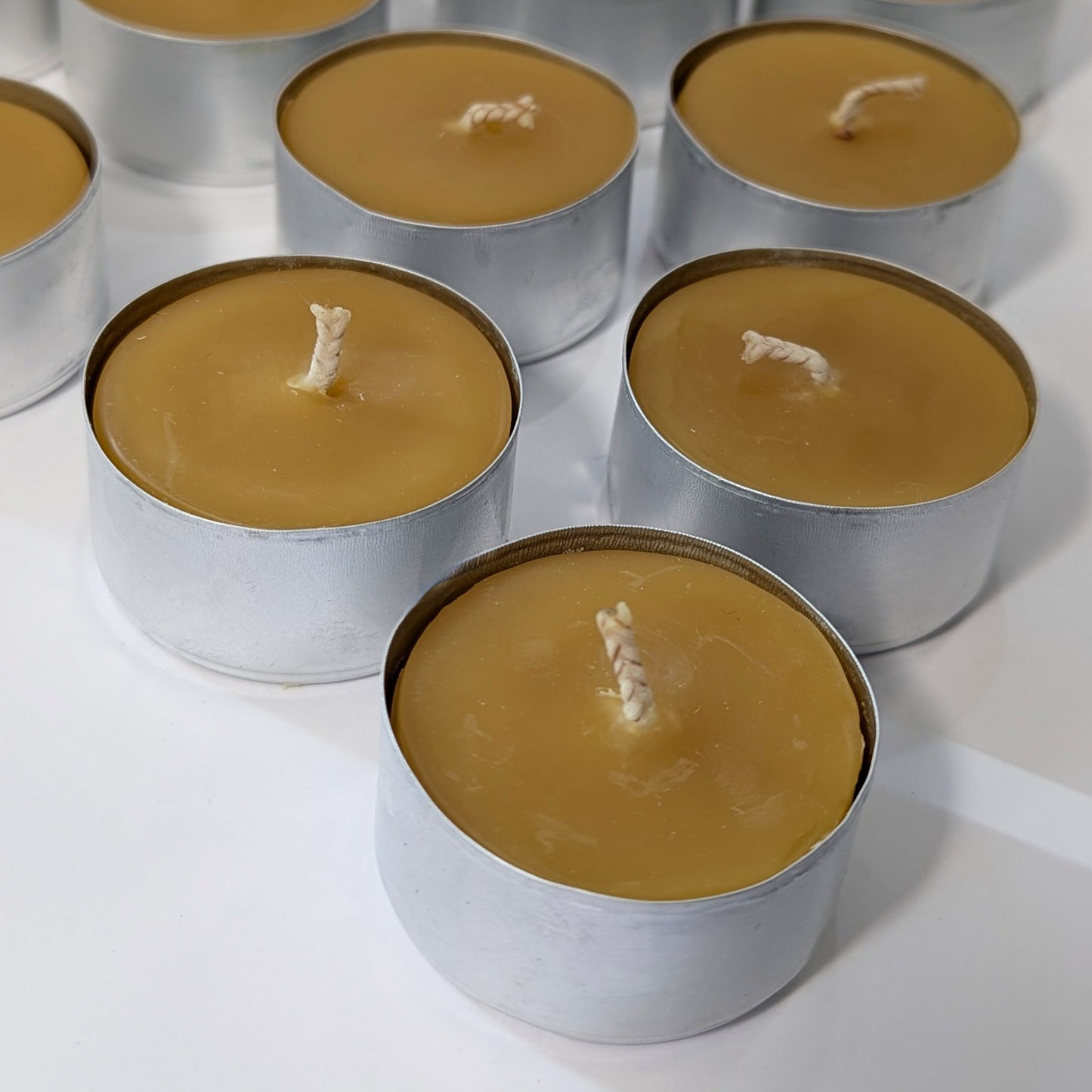 Close-up view of multiple pure beeswax tealights in metal cups, highlighting natural texture, golden color, and sturdy cotton wicks.