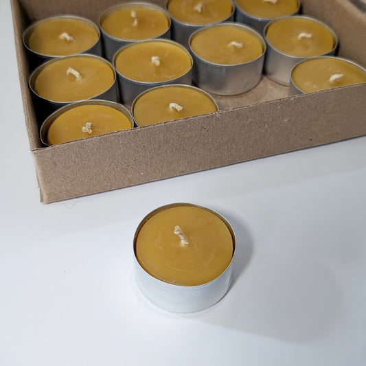 Pure beeswax tealight candle set with one tealight displayed in front of an open box of twelve, showing golden beeswax and metal cups.