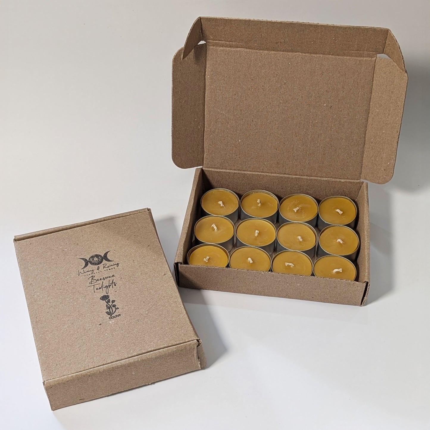 Pure beeswax tealight candle set of twelve displayed in an open Kraft box with additional closed packaging beside it, showcasing eco-friendly presentation.