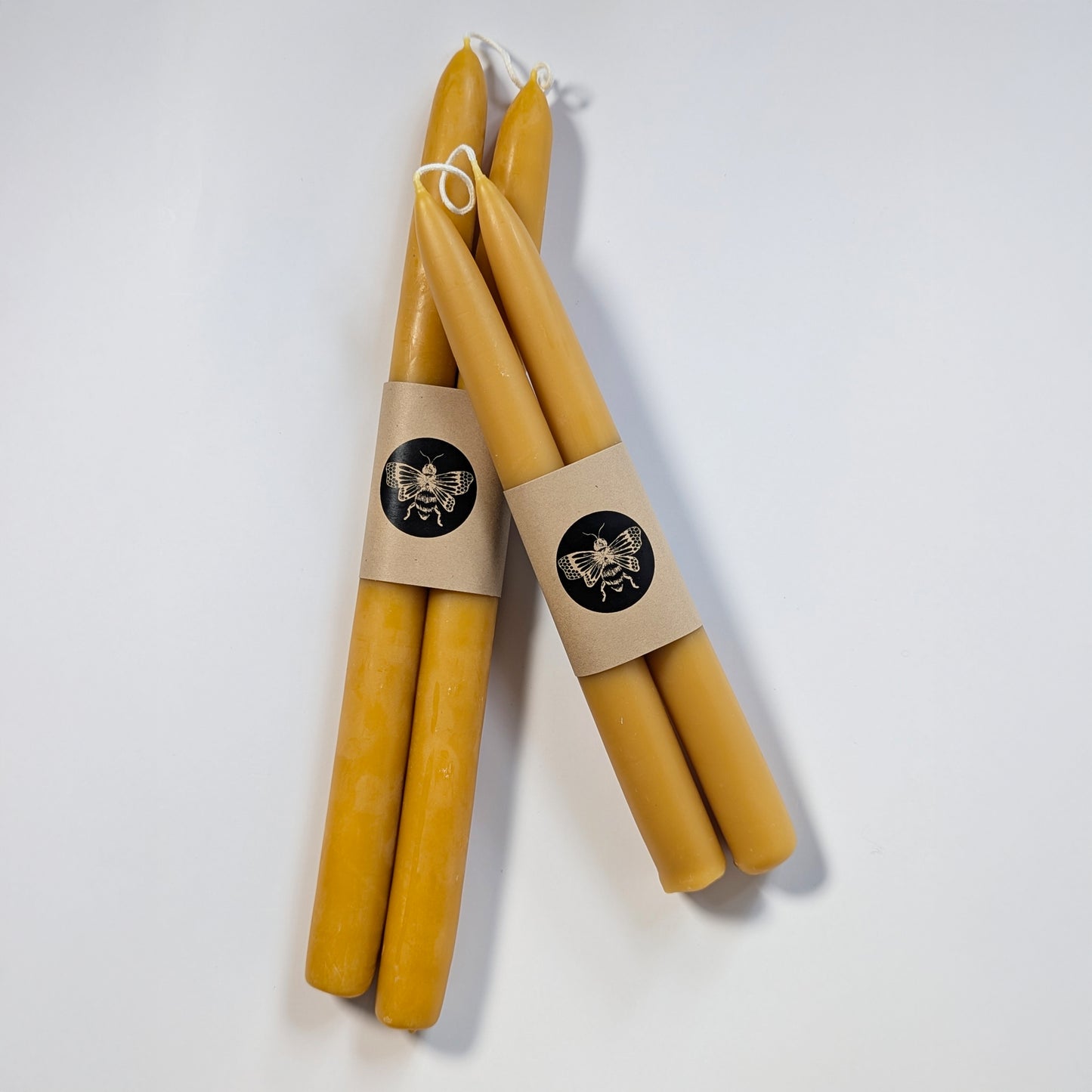 Set of handcrafted pure beeswax candlesticks wrapped in Kraft paper with a bee seal, highlighting their natural finish and artisanal presentation.